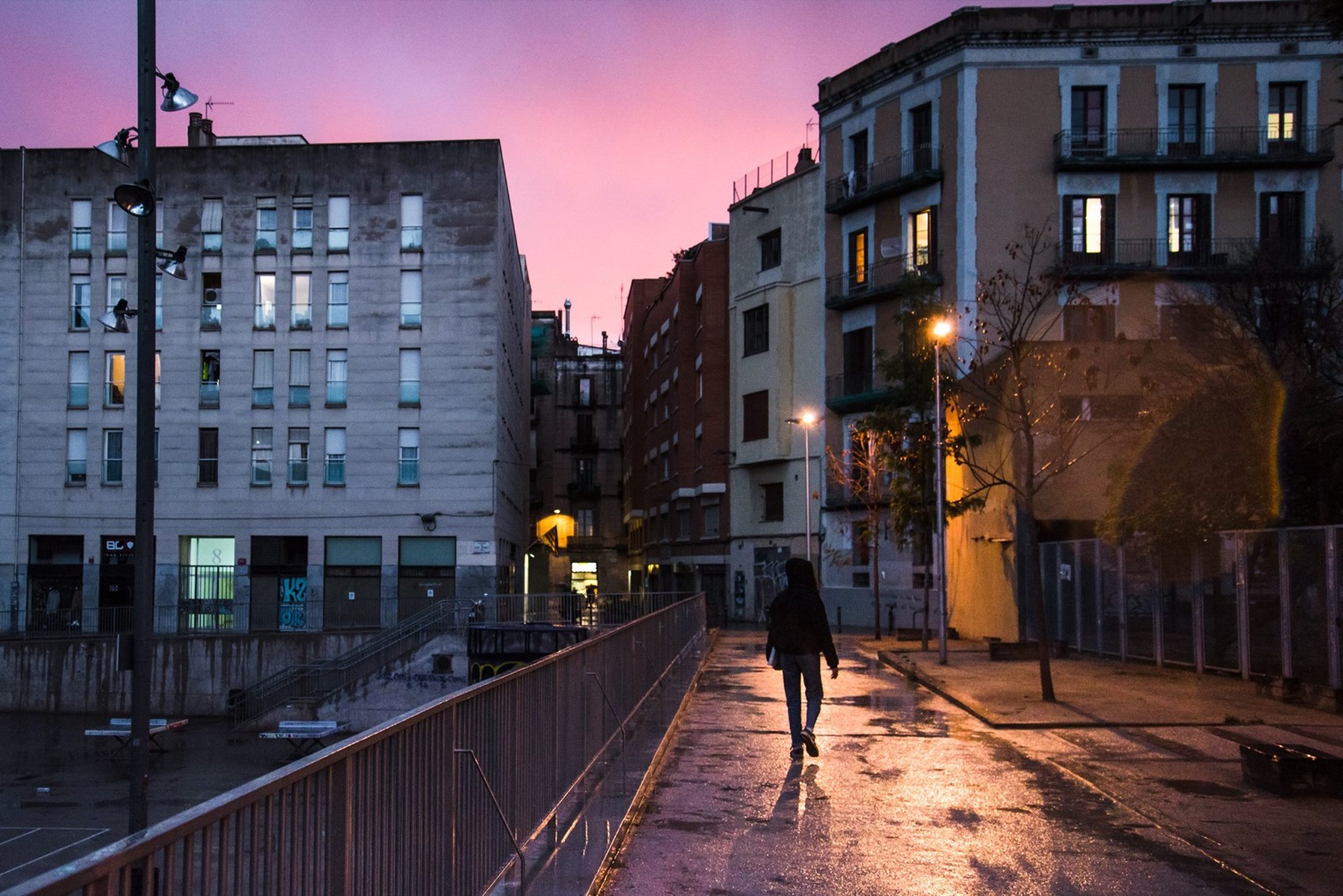 A lone figure walking a wet street at dusk in Barcelona.